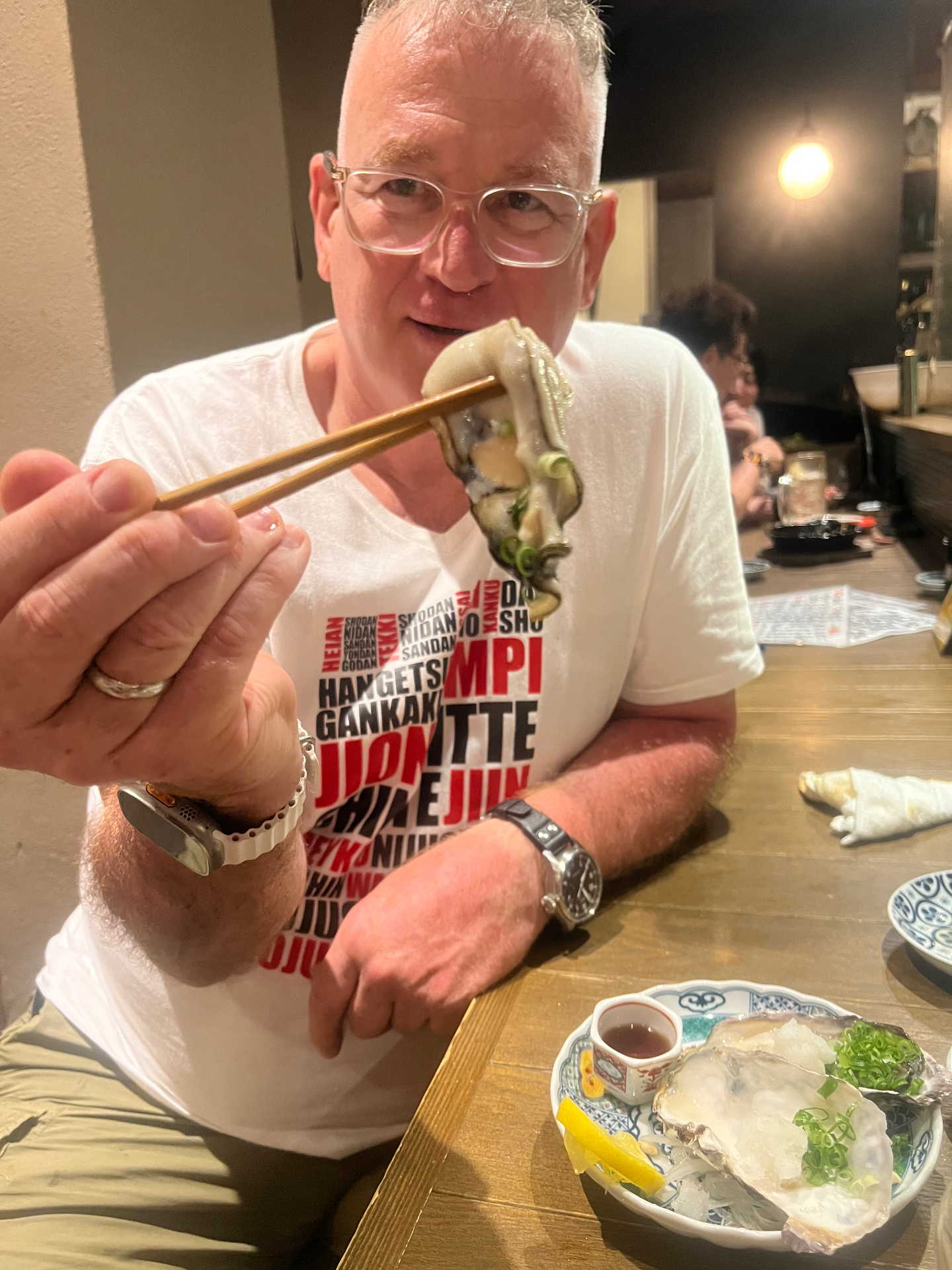 Karateka in JKA-Shirt isst eine frische Auster mit Stäbchen in einer Izakaya