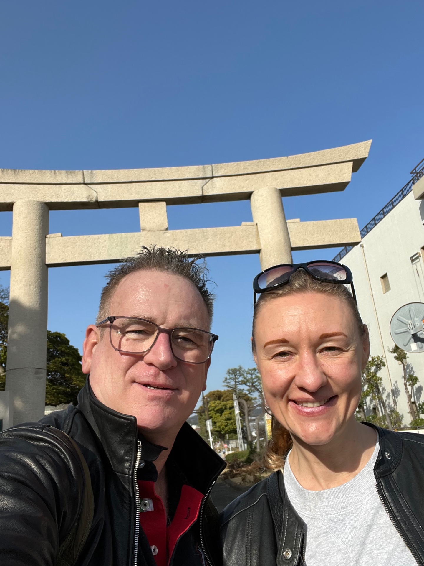 Selfie zu zweit vor einem großen steinernen Torii unter strahlend blauem Himmel